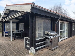 Un espace extérieur abrité, équipé d’un barbecue, d’une table avec des chaises et offrant une vue sur les environs.