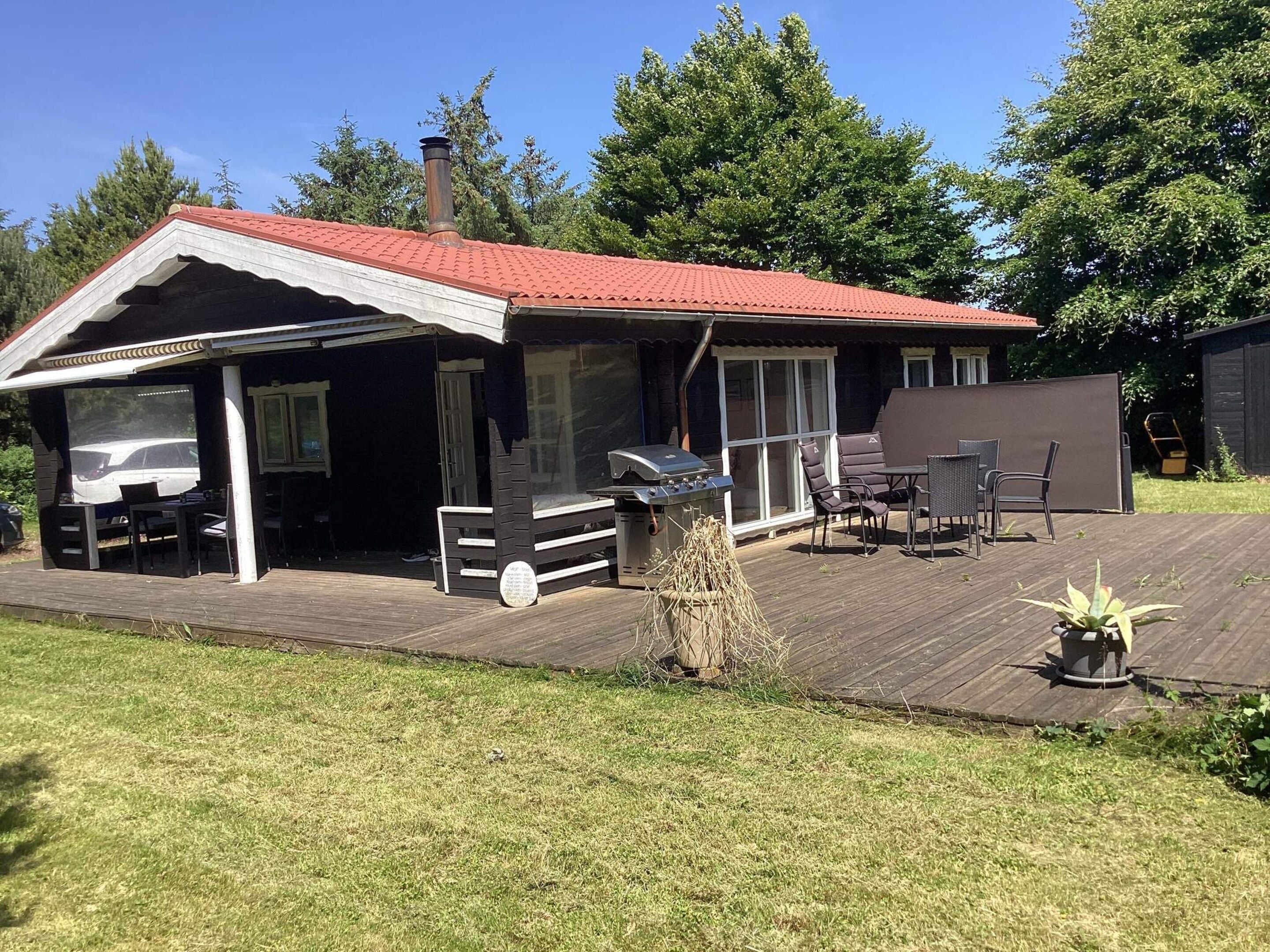 A covered outdoor area with a barbecue grill, seating, and a view of the house.