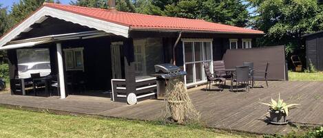 A covered outdoor area with a barbecue grill, seating, and a view of the house.
