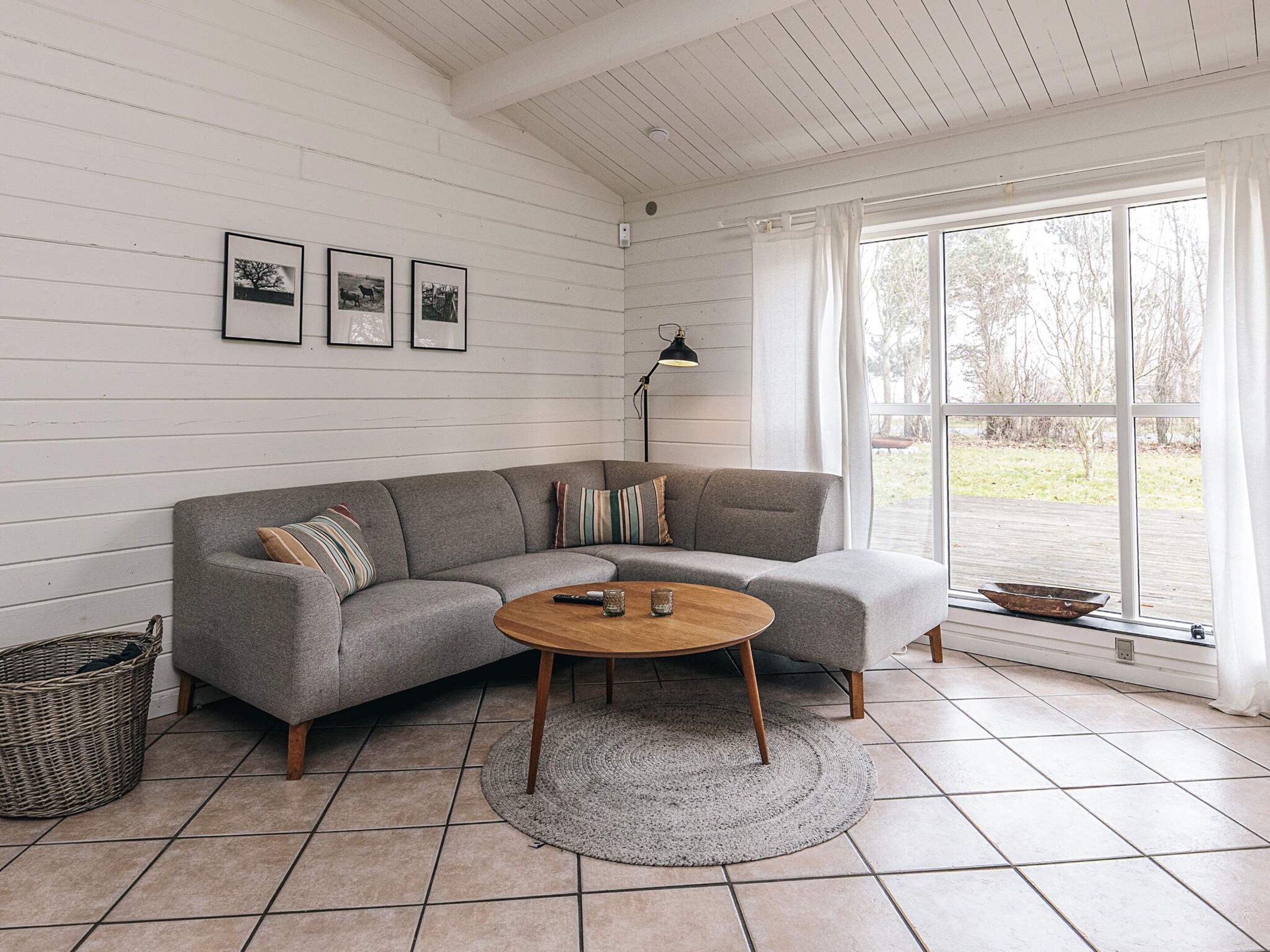 A living room with a grey sectional sofa, a round coffee table, a floor lamp, and a large window with curtains.