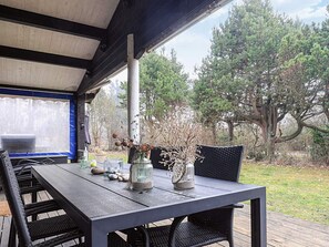 An outdoor patio with a table and chairs, surrounded by trees and a covered area. - 5 Person Holiday Home in Nakskov (Nakskov)