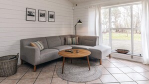 A living room with a grey sectional sofa, a round wooden coffee table, a floor lamp, and a large window with curtains.