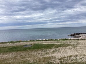 A coastal landscape with a rocky shoreline, a grassy foreground, and a calm sea under a cloudy sky. - 5 Person Holiday Home in Nakskov (Nakskov)