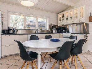 A modern kitchen with white cabinets, a round dining table, black chairs, and a stainless steel range hood. - 5 Person Holiday Home in Nakskov (Nakskov)