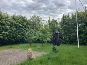 A grassy outdoor area with a wooden deck, a covered structure, and dense foliage in the background. - 5 Person Holiday Home in Nakskov (Nakskov)