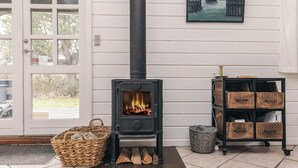 A room with a wood-burning stove, a wicker basket, a metal shelf with wooden boxes, and a door with a glass panel.