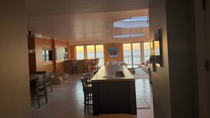 Una cocina amplia con una isla grande, comedor con sillas y vista al mar a través de ventanas grandes.