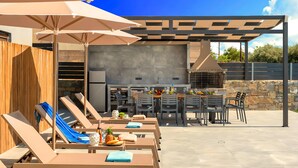 Une terrasse extérieure avec des chaises longues, un espace barbecue et un mur en pierre en arrière-plan.