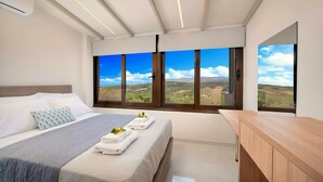 Une chambre à coucher moderne, dotée d’un grand lit, d’un bureau en bois et offrant une vue sur un paysage grâce à de grandes fenêtres.
