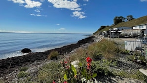 A coastal view with a clear sky, a rocky shoreline, and a building with outdoor seating. - 4 Person Holiday Home in Kopingebro (Köpingebro)