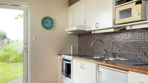 A kitchen with white cabinets, a microwave, a sink, and a clock on the wall. - 4 Person Holiday Home in Kopingebro (Köpingebro)