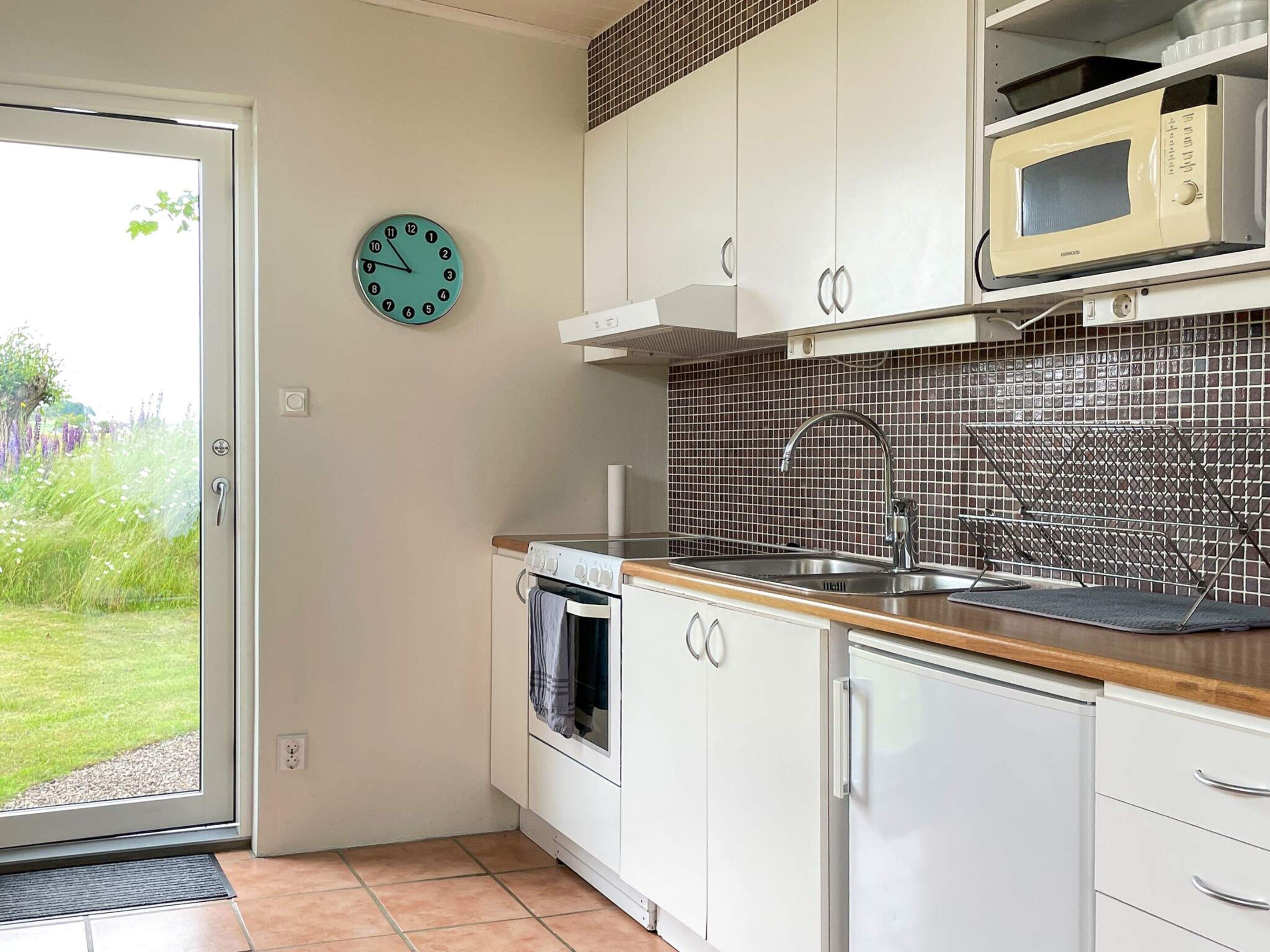 A kitchen with white cabinets, a microwave, a sink, and a clock on the wall.