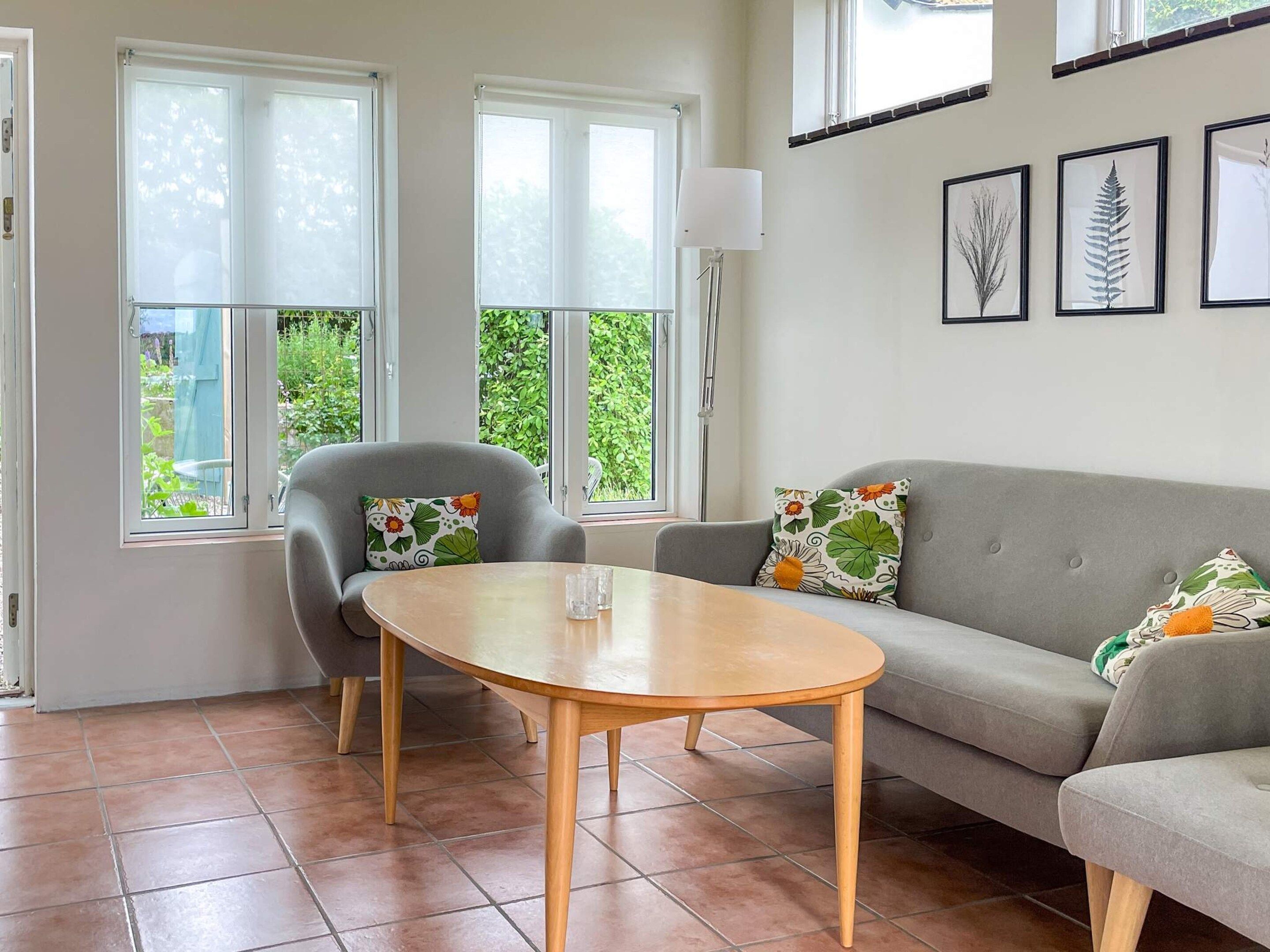 A living room with a grey sofa, a grey armchair, a round wooden table, and a glass of water.