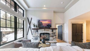 A living room with a stone fireplace, a large window, and a television mounted above it. - Catamount Lodge 101 - 2 Bedroom (Truckee)