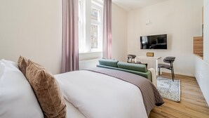 A modern hotel room with a large bed, a desk, a television, and a view of a building outside. - Blueground | Letná, museums, foodie area (PRG-56) (Prague)