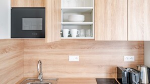 A modern kitchen with wooden cabinetry, a built-in oven, and a countertop with a kettle, toaster, and coffee maker. - Blueground | Letná, museums, foodie area (PRG-56) (Prague)