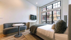 A modern bedroom with a bed, a sofa, a small round table, and a TV on the wall. - Catamount Lodge 101A -  Studio (Truckee)