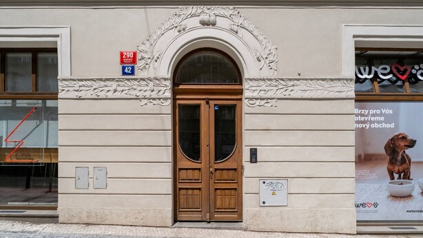Une façade d’immeuble avec une porte à double battant en bois, une plaque et un panneau indiquant l’emplacement d’un arrêt de bus à proximité.