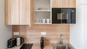 Une cuisine moderne avec des meubles en bois, un réfrigérateur noir, un évier, un grille-pain, une bouilloire et une machine à café.