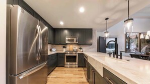 Une cuisine moderne dotée d’appareils électroménagers en acier inoxydable, de meubles de rangement aux couleurs sombres et d’un plancher en bois.