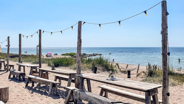 A beach with wooden picnic tables and string lights, overlooking the ocean. - 4 Person Holiday Home in Klintehamn (Klintehamn)