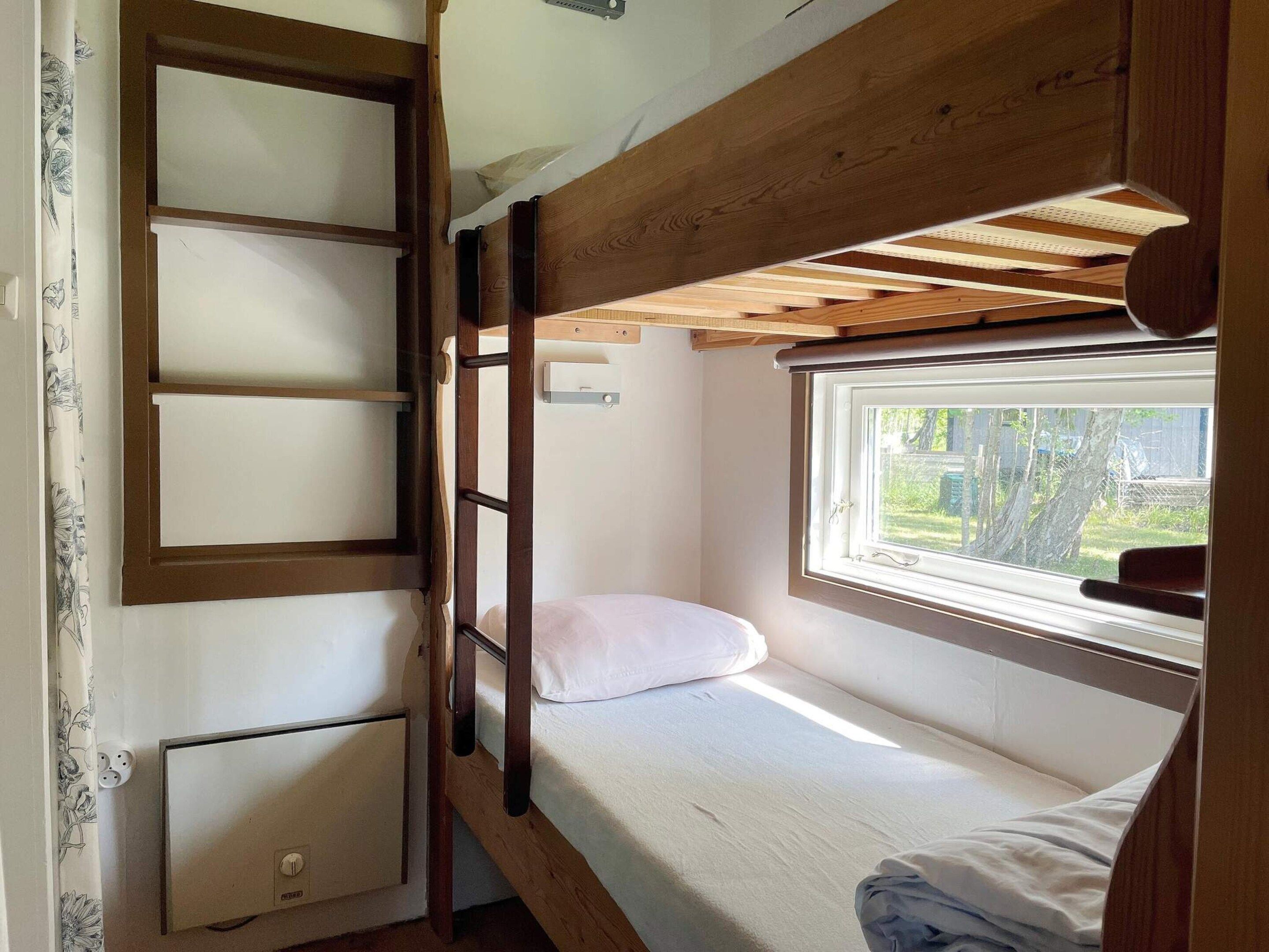Un lit superposé avec une fenêtre, une table de chevet et une prise de courant.