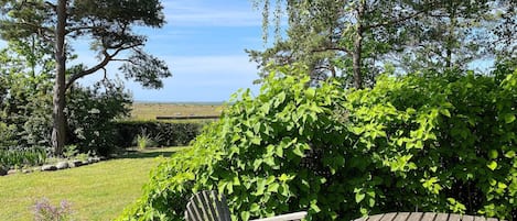 A wooden deck with two chairs and a table, surrounded by lush greenery and a view of the countryside.