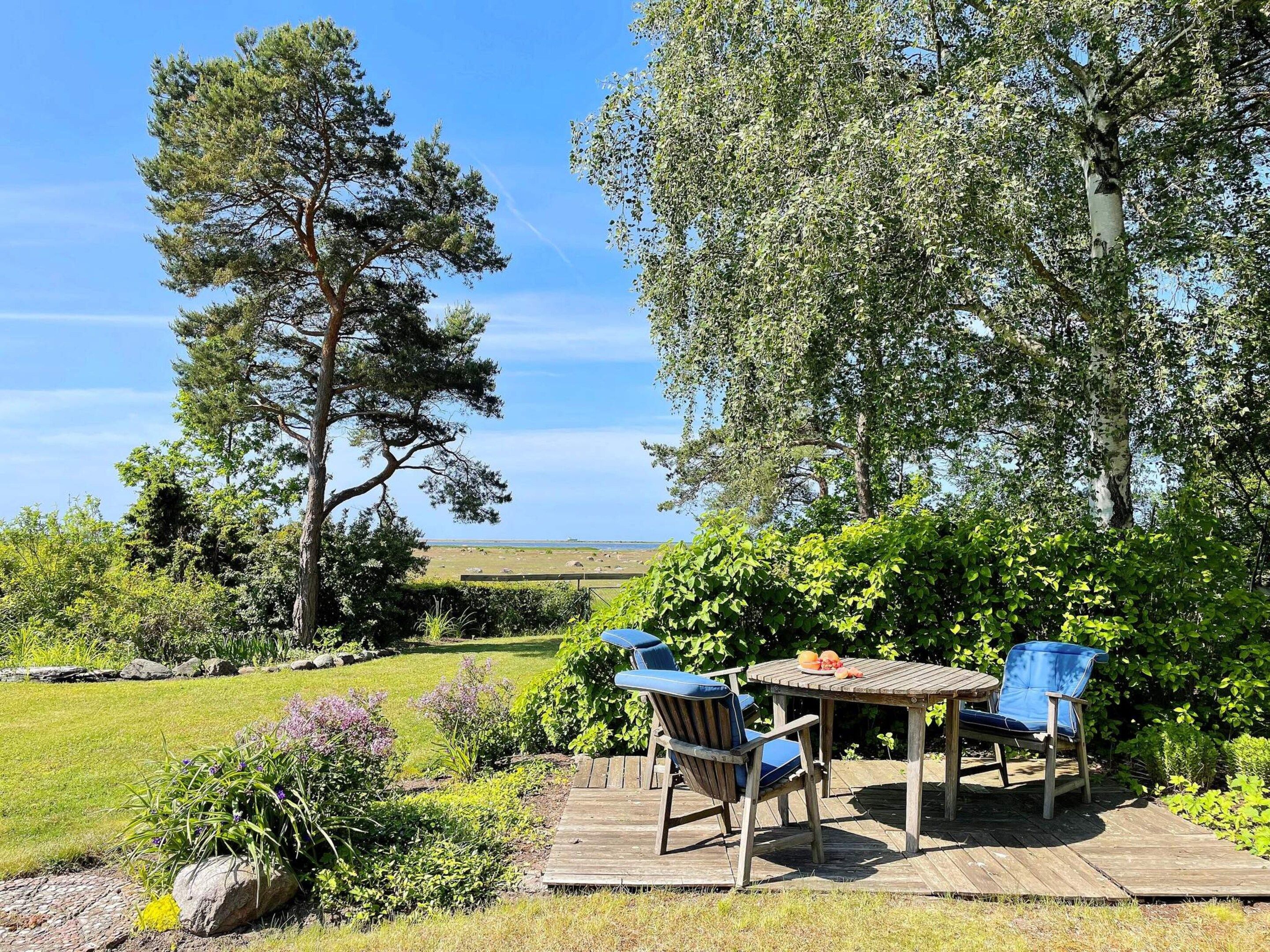 Une terrasse en bois avec deux chaises et une table, entourée d’une végétation luxuriante et d’arbres.