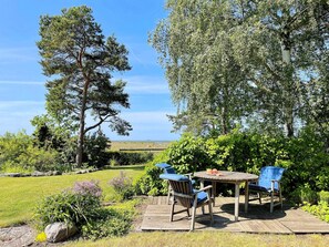 A wooden deck with two chairs and a table, surrounded by lush greenery and trees. - 4 Person Holiday Home in Klintehamn (Klintehamn)