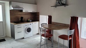Eine kleine Küche mit Waschmaschine, Kaffeemaschine und Essbereich mit zwei Stühlen und einem Tisch.