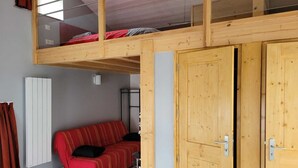 Ein Zimmer mit einem Etagenbett, einem roten Sofa, einem Heizkörper und Holztüren.
