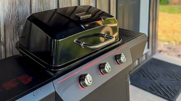 Una parrilla exterior negra con tres quemadores y una pantalla digital, ubicada frente a una puerta de madera.