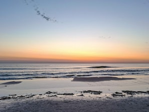 Ein Strand mit Wellen, blauem Himmel und einem Sonnenuntergang.