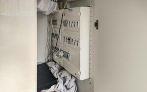 Ein Verteilerkasten mit zahlreichen Schaltern und Kabeln, einem Türgriff und einer weißen Wand.