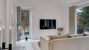 Una sala de estar moderna con un sofá, un televisor de pantalla plana y vistas a través de amplios ventanales.