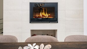 Una chimenea moderna con una pantalla de televisión, una mesa de comedor con sillas y un adorno de pared decorativo.