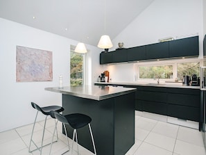 A modern kitchen with a central island, black bar stools, and pendant lighting. - 5 Star Holiday Home in Blokhus (Blokhus)