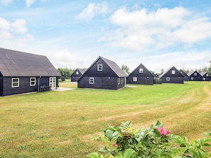 A row of dark-colored, single-story buildings with a flat roof, arranged in a linear fashion on a grassy field. - 5 Star Holiday Home in Farso (Farso)