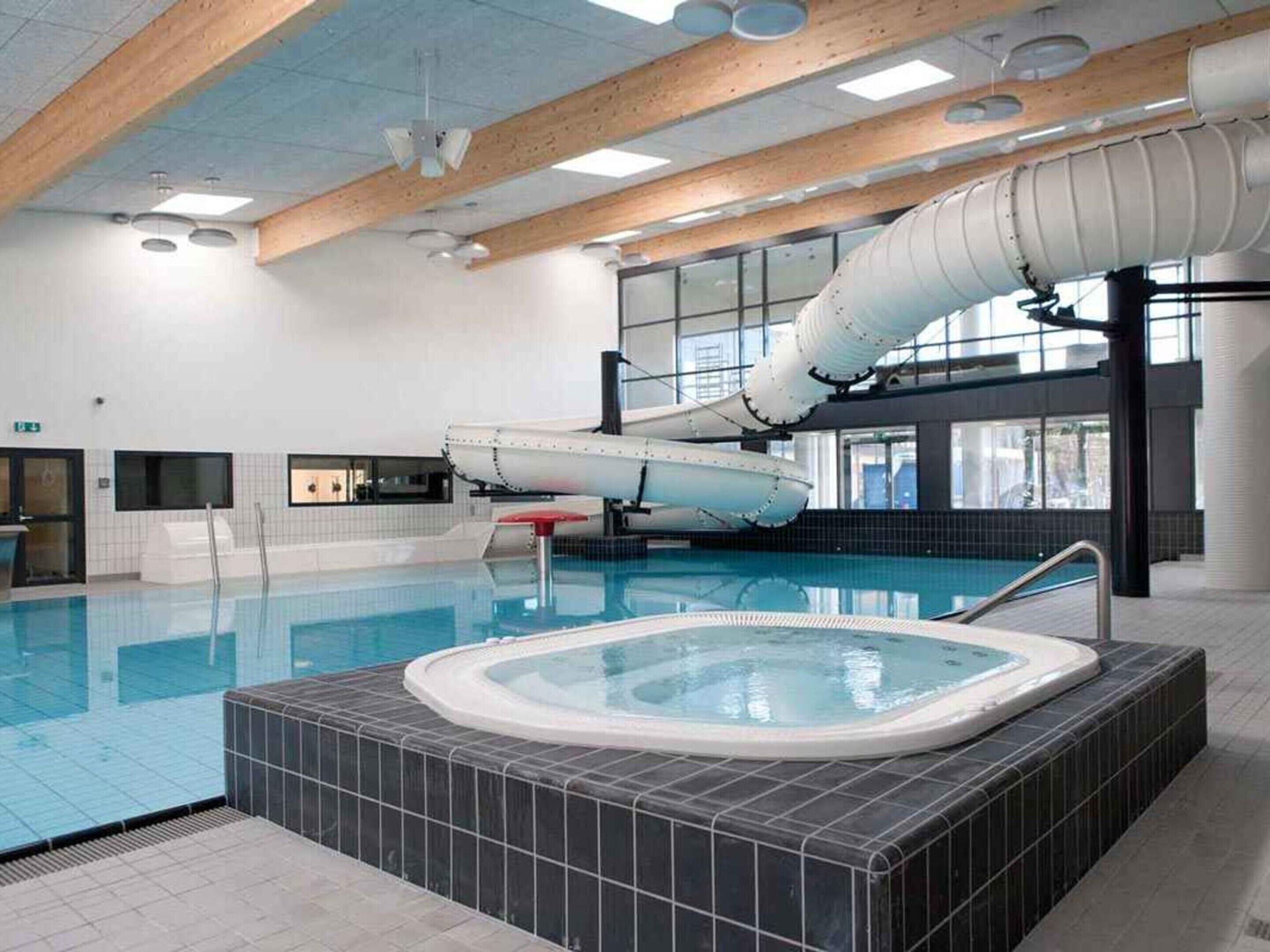 An indoor swimming pool with a hot tub, wooden beams, and large windows.