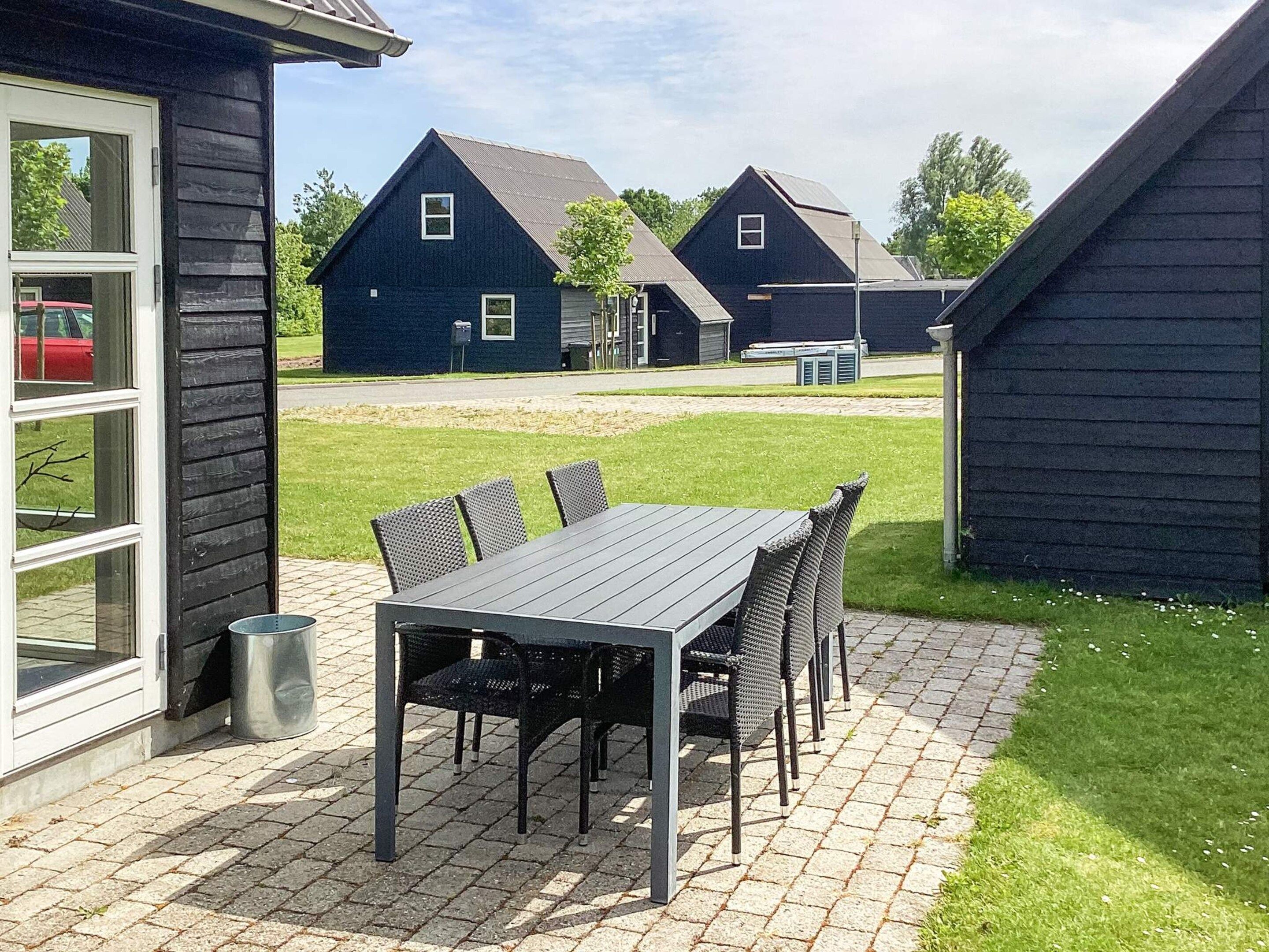 A patio with a table and chairs, a trash can, and a building with a dark exterior.