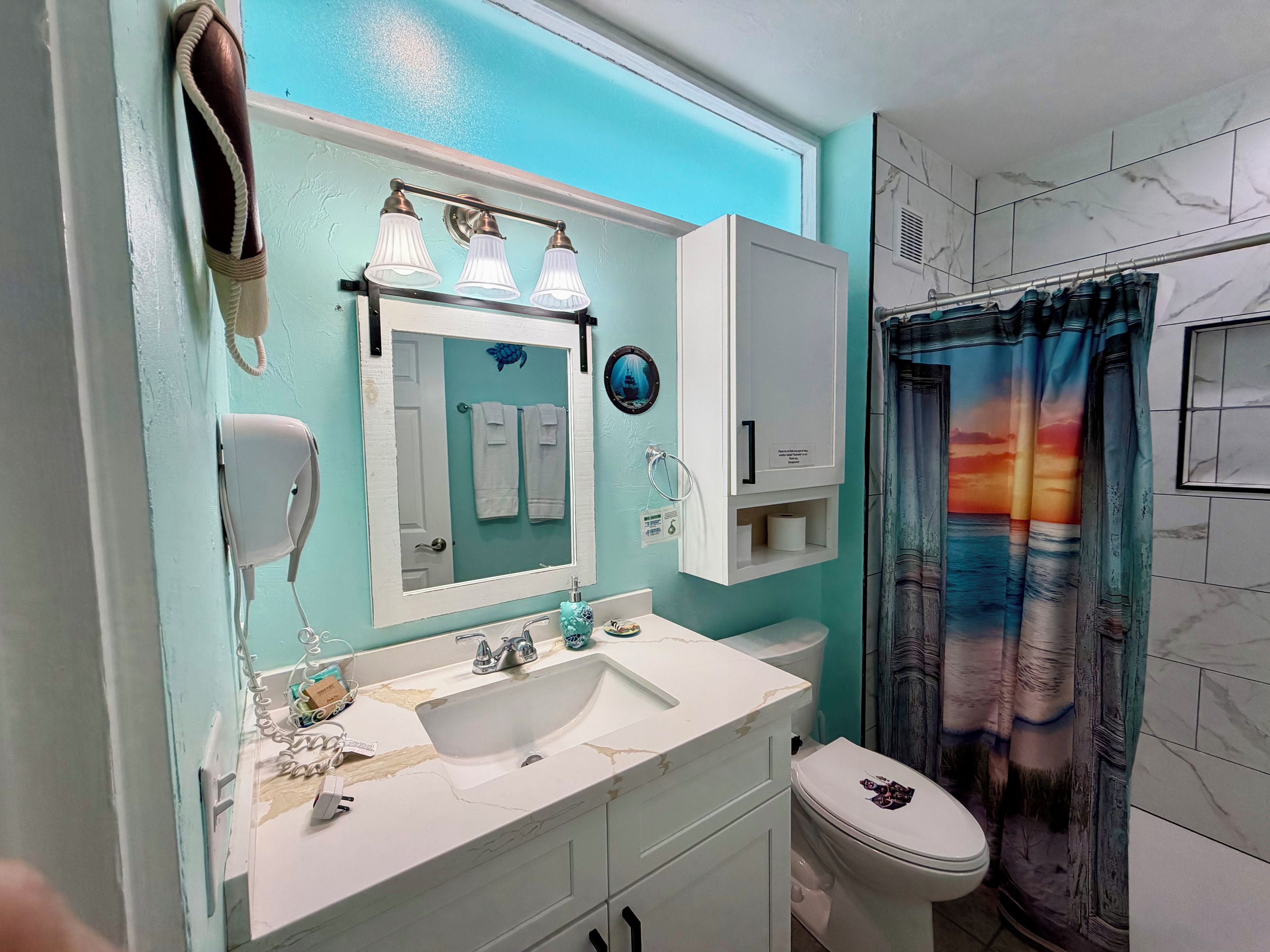 A bathroom with a white sink, a mirror, a towel rack, a toilet, and a shower curtain with a sunset design.
