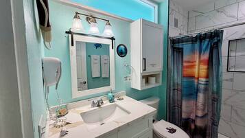 A bathroom with a white sink, a mirror, a towel rack, a toilet, and a shower curtain with a sunset design.