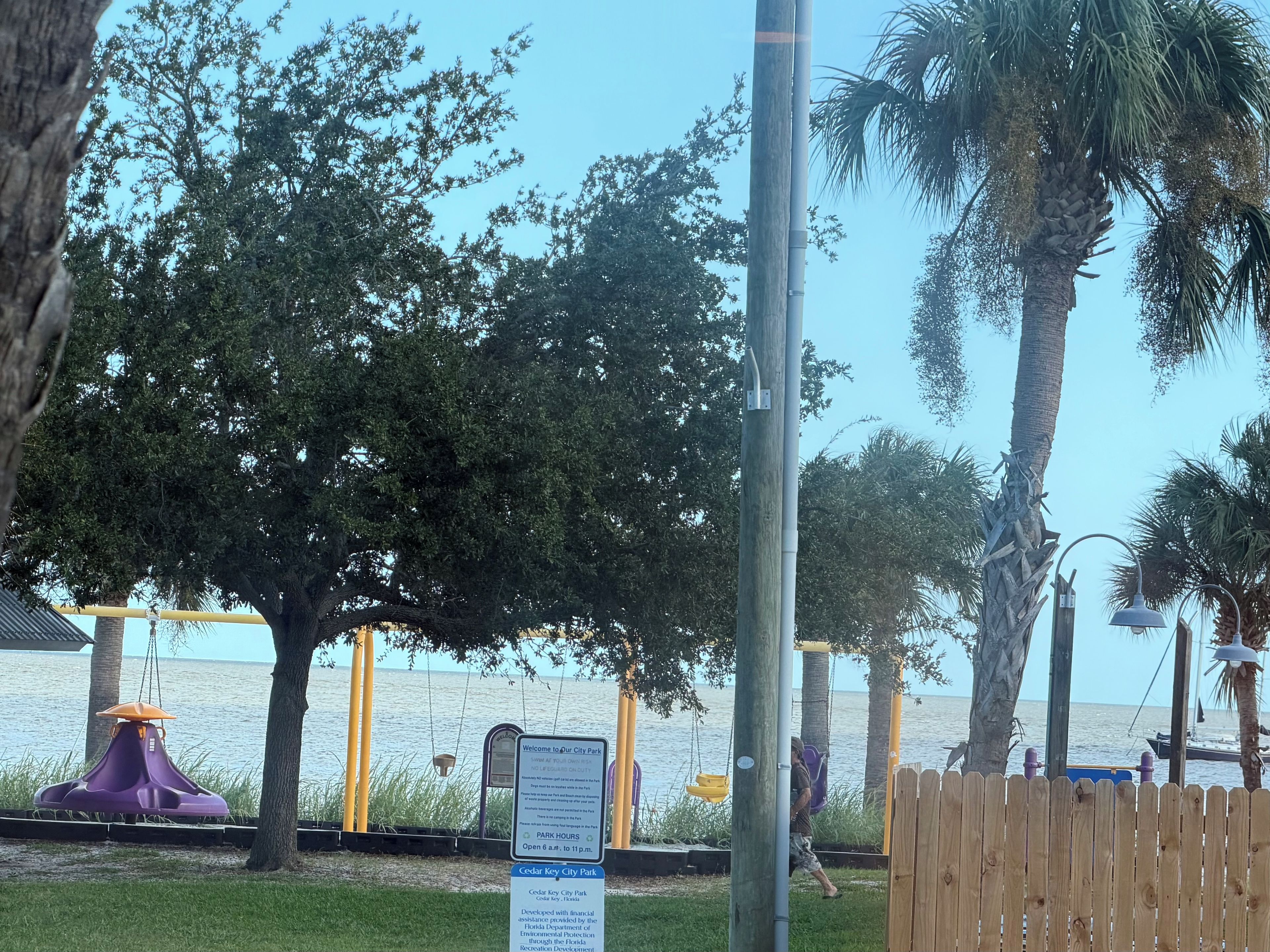 A park with a swing set, a wooden fence, and a signboard.