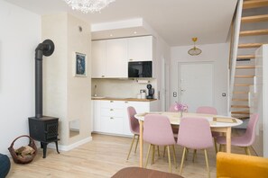 A modern kitchen with white cabinets, a black stove, and a dining area with pink chairs and a wooden table.