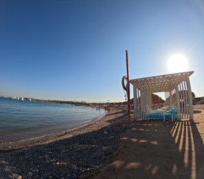 A beach with a wooden structure and lounge chairs.