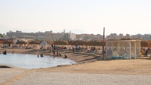 Una playa con gente, cabañas de techo de paja y un camino pavimentado.