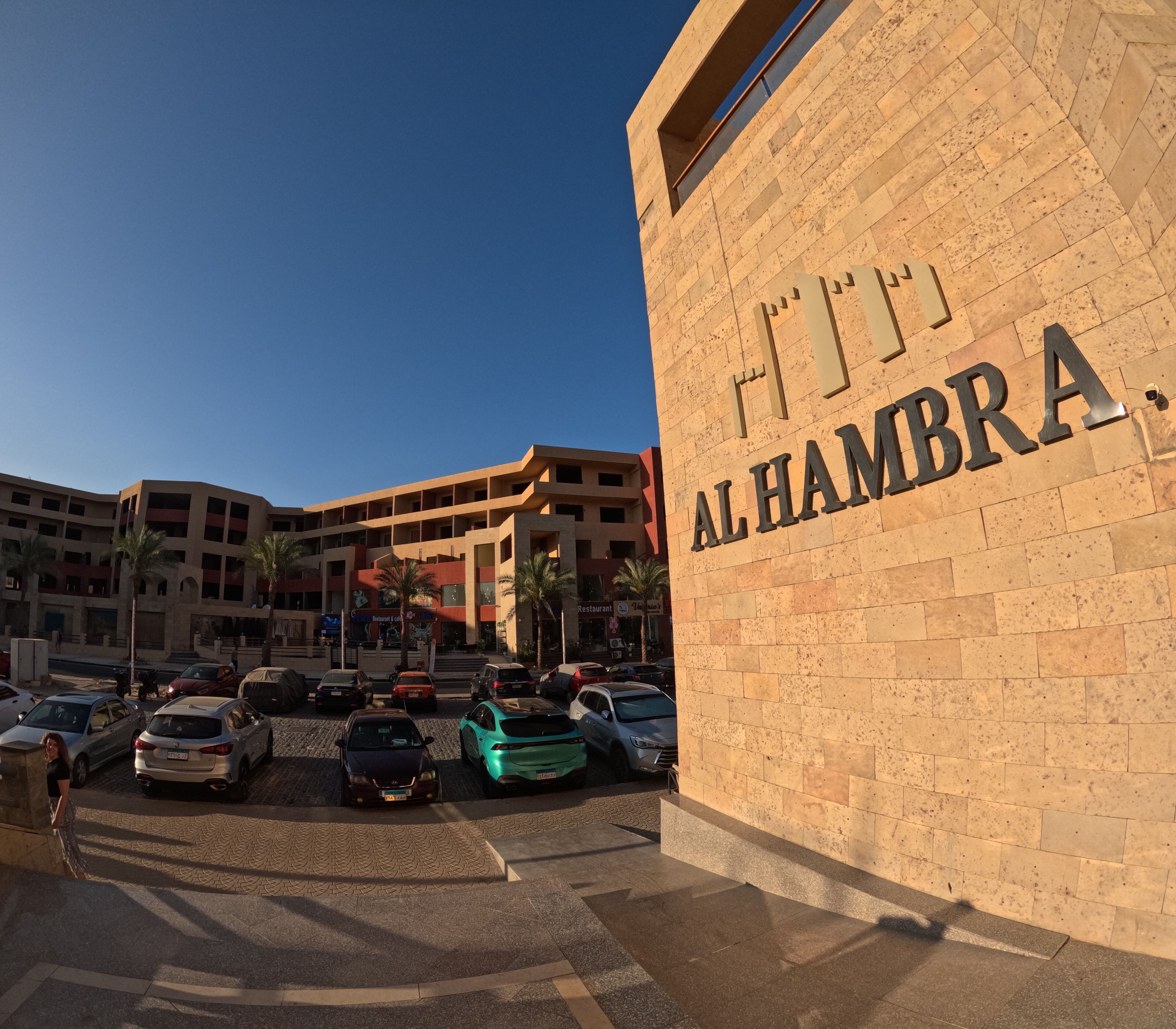 Un edificio con il cartello "AL HAMBRA" e un'area di parcheggio con diverse automobili.