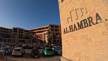 Un edificio con el letrero "AL HAMBRA" y un estacionamiento con varios automóviles.