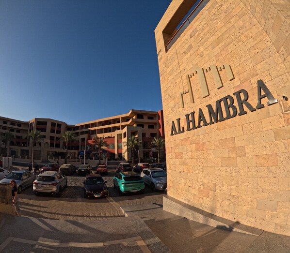 A building with the sign "AL HAMBRA" and a parking area with various cars.