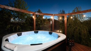 A hot tub on an outdoor deck with string lights and trees in the background.